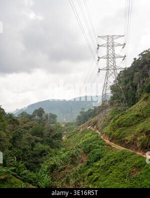 Tanah Rata, Cameron Highlands, Malaysia – 27. Januar 2020: Übertragungsturm und Stromleitungen über einem Feldweg, der durch grüne Hügel führt. Stockfoto