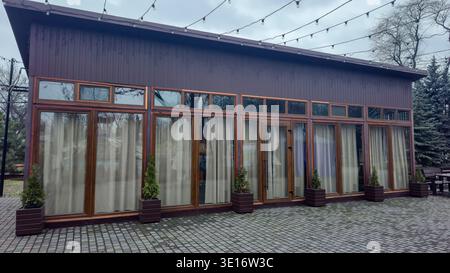 Ein modernes Restaurantgebäude mit Panoramafenstern und Holzwänden in einem Stadtpark. Die Terrasse ist mit Girlanden dekoriert. Die Atmosphäre schafft einen Stockfoto