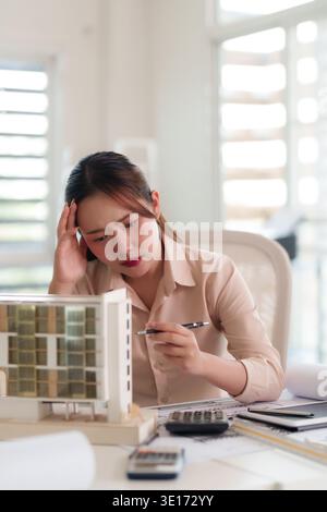 Besorgte Architektin untersucht kompliziertes Baumodell. Sie plant Entwicklung und überwindet Designschwierigkeiten in ihrem professionellen Arbeitsbereich. Stockfoto