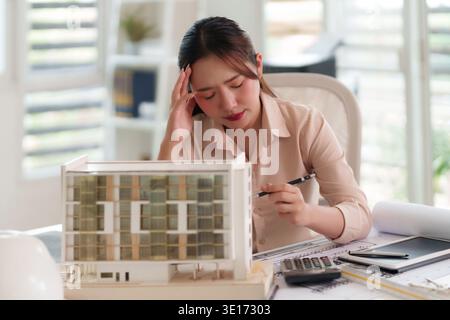 Asiatischer Architekt spürt Arbeitsdruck bei der Prüfung von Bauplänen für Architekturmodelle Projekttermin Stress Design Kreativität Problemlösung Stockfoto