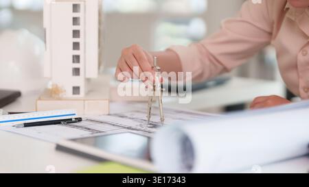 Erfahrene Hand für Erwachsene mit Präzisionskompass auf architektonischen Bauplänen. Gestaltung moderner Baustrukturen und städtebaulicher Projekte. Stockfoto