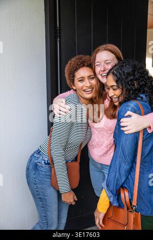 Verschiedene Freundinnen umarmen sich gegenseitig und lächeln am Hauseingang mit Ledertaschen. Freundschaft, Gemeinschaft, Vielfalt, Lebensstil, Wärme, Gesellschaft, Mode || Model veröffentlicht Stockfoto