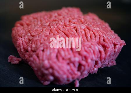 Eine hochwinklige Kinoaufnahme betont die frische Textur von rohem, gemahlenem Rindfleisch, das zum Kochen bereit ist. Die geringe Tiefe des Feldes erzeugt ein appetitliches und Stockfoto