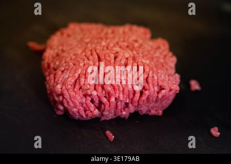 Eine hochwinklige Kinoaufnahme betont die frische Textur von rohem, gemahlenem Rindfleisch, das zum Kochen bereit ist. Die geringe Tiefe des Feldes erzeugt ein appetitliches und Stockfoto