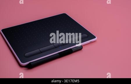 Modernes Grafiktablett mit Eingabestift auf weichem rosa Hintergrund. Digitales Zeichengerät für Designer und Künstler, die im Kreativstudio envi arbeiten Stockfoto