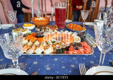Ein festlicher Esstisch mit einer großen Platte mit Sushi als Herzstück, mit Lachs-Sashimi, Maki-Rollen, Garnelen-Nigiri und Stockfoto