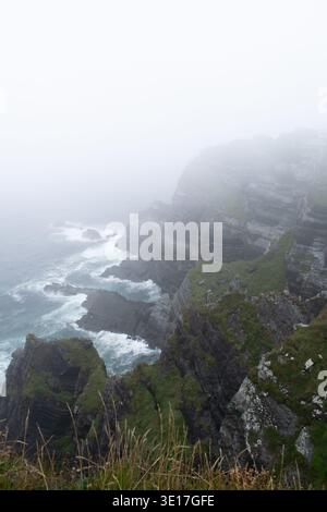 Ring of Kerry Klippen an einem nebeligen Tag mit vielen Wolken und Nebel. Scharfe Berge neben einem aufgewühlten Meer Stockfoto