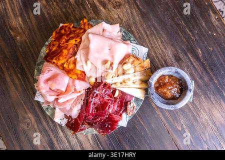 Eine rustikale Wurstplatte mit verschiedenen geräucherten Schinken, Käse und Nüssen, wunderschön auf einem Holztisch angeordnet, perfekt für Gourmet-Präsentationen oder Stockfoto