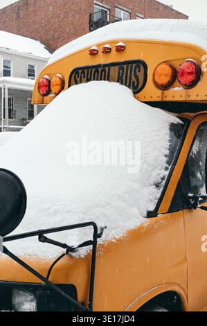 An einem kalten Wintertag in Brooklyn, USA, sitzt ein Schulbus im Leerlauf, bedeckt mit schwerem Schnee. Das leuchtende Gelb bildet einen Kontrast zum weißen Schnee und schafft so eine se Stockfoto