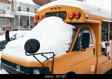 Ein gelber Schulbus parkt auf einer verschneiten Straße in Brooklyn, USA, mit frischem weißem Schnee. Leuchtend rote Lichter und ein Stoppschild sind auf dem zu sehen Stockfoto
