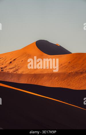 Goldene Farbtöne zeichnen Dune 45 aus, ein markantes Wahrzeichen in Namibias Namib-Wüste. Die anmutigen Kurven und die aufragende Präsenz schaffen wieder eine atemberaubende Silhouette Stockfoto