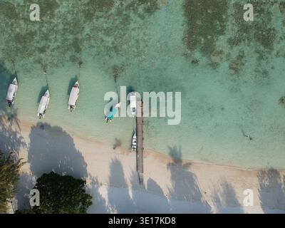 Atemberaubende Aussicht auf traditionelle Boote, die auf kristallklarem türkisfarbenem Wasser in der Nähe eines hölzernen Piers auf den perhentischen Inseln in malaysia schwimmen Stockfoto