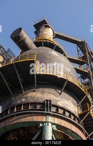Eine große industrielle Metallkonstruktion mit komplizierten Details und gelben Sicherheitsgeländern, die robuste Technik vor einem klaren blauen Himmel zeigt, symbolisiert Stockfoto