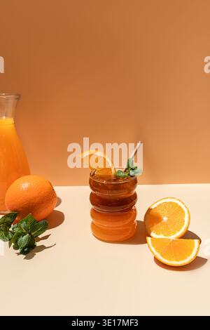 Erfrischende, eiskalte Zitrus americano serviert in einem einzigartigen welligen Glas mit einer frischen Orangenscheibe. Begleitet von einer ganzen Orange, Minzblättern und einem Krug oran Stockfoto