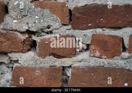 Makrostruktur einer alten roten Ziegelwand mit grauem Betonmörtel. Detailansicht der verwitterten und beschädigten Mauerwerksoberfläche mit sichtbaren Lücken Stockfoto