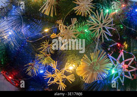 Strohweihnachtsschmuck am Baum. Rustikale Dekoration am Weihnachtsbaum. Mehrfarbige Garland-Leuchten Stockfoto
