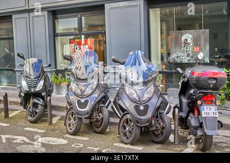 – 19. MÄRZ 2026: Vier Motorroller, die auf einer Kopfsteinpflasterstraße in Paris, Frankreich, vor einem grauen Ladengeschäft mit großen... Stockfoto