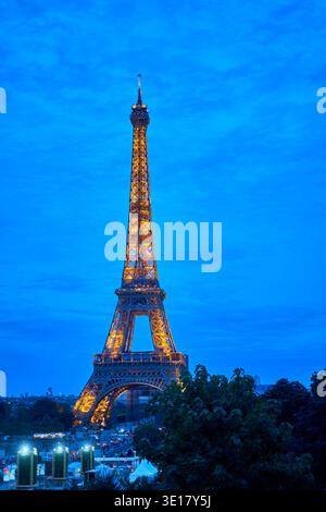 Der Eiffelturm steht majestätisch vor einem tiefblauen Abendhimmel, der von tausenden goldenen Lichtern beleuchtet wird, die seine komplizierte... Stockfoto