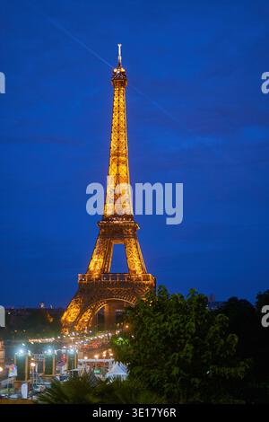 Der Eiffelturm steht majestätisch beleuchtet vor einem tiefblauen Abendhimmel in Paris, Frankreich. Die ikonische Eisengitterstruktur leuchtet mit... Stockfoto