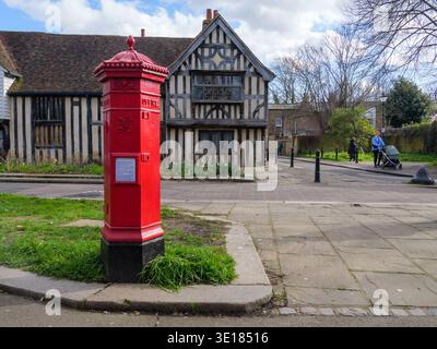 Ein seltener viktorianischer Penfold-Säulenkasten steht an der Church Lane in Walthamstow Village, London, im März 2026. Dieser ikonische sechseckige Briefkasten, der von dem Architekten John Wornham Penfold entworfen und zwischen 1866 und 1879 hergestellt wurde, ist einer von nur wenigen originalen „Penfolds“, die in der Hauptstadt noch in Gebrauch sind. Die Box verfügt über eine unverwechselbare Kappe mit Akanthusblättern, einer Knospe und dekorativen Kugeln. Im Hintergrund befindet sich das Ancient House, ein denkmalgeschütztes Fachwerkhaus aus dem Jahr 1435, was es zu einem der ältesten erhaltenen Wohngebäude Londons macht Stockfoto