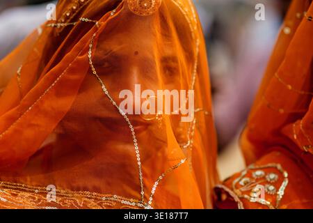 Eine Nahaufnahme einer jungen Frau in Pushkar Mela, die einen orangefarbenen, durchscheinenden Schleier mit silbernen Pailletten und einem goldenen Nasenring trägt. Stockfoto