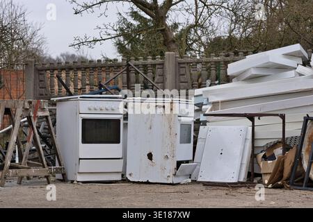 Alte, rostige Gasöfen und weiße Sperrmüll, die draußen in der Nähe eines Betonzauns gelagert werden. Elektronikschrott und -Schrott Stockfoto