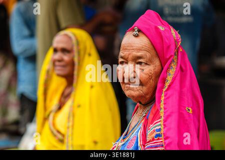 Eine ältere Frau in Pushkar Mela mit rosa Kopftuch schaut zur Seite, während eine Frau in Gelb hinter ihr sitzt. Stockfoto