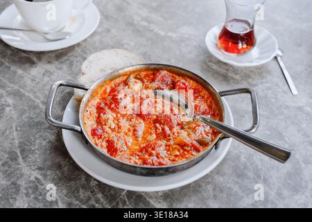 Traditionelle Shakshuka mit pochierten Eiern in würziger Tomatensauce, serviert in einer Metallpfanne mit Brot und türkischem Tee auf dem Tisch, Essensküche, Frühstück Stockfoto