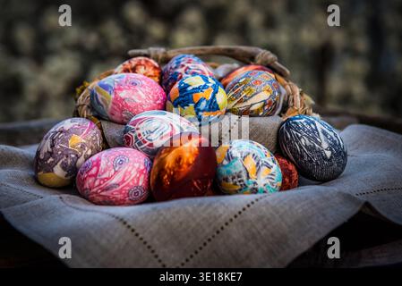Eine Sammlung dekorativer seidengefärbter Ostereier in einem rustikalen Webkorb auf einem Leinentuch. Stockfoto