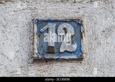Altes Metallhaus-Nummernschild an der strukturierten Wand mit Details aus urbaner Architektur und historischer Adresse. Stockfoto