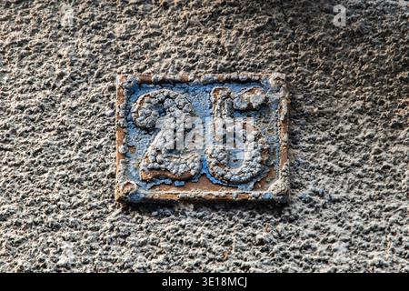 Verwittertes Metallhaus Nummer 25 auf der rauen Wand mit Vintage-Architekturdetails und urbaner Straßenmarkierung. Stockfoto