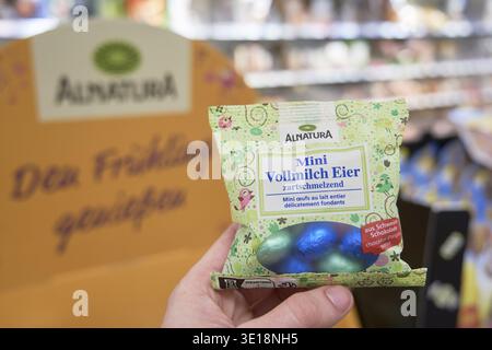 Alnatura Mini Vollmilcheier, farbenfrohe Verpackung hält zwei Schokoladeneier, verschwommene Ladenatmosphäre im Hintergrund, Bio-, Ostern-, Oster- und Osterschokola Stockfoto