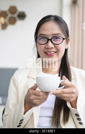Junge asiatische Geschäftsfrau, die im Café-Restaurant sitzt, Anzug und Brille trägt und Kaffee trinkt Stockfoto