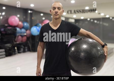 Glatze Hispanic man trainiert im Fitnessstudio für Fitness und Pilates-Workout. Muskulöser Mann, der zuversichtlich drinnen trainiert, mit schwarzem Hemd. Gesundes Leben Stockfoto