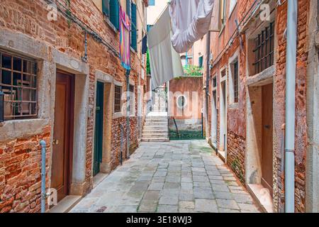 Venedig enge Straße mit historischen Backsteinhäusern und hängender Wäscherei in der traditionellen italienischen Stadt Veneto, Italien. Traditionelle venezianische Architektur Stockfoto