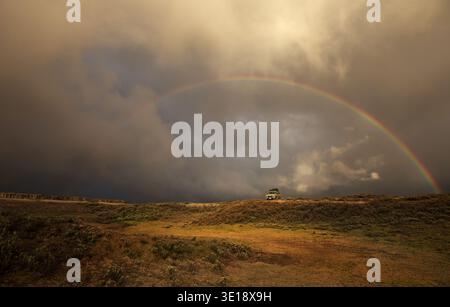 Ein einsamer Geländewagen steht auf einem abgelegenen Bergrücken unter einem hellen Regenbogen vor dunklen Sturmwolken in der weiten Wildnis Äthiopiens. Stockfoto