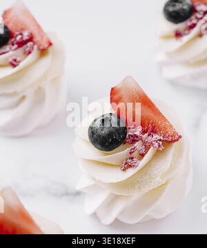 Die Mini-Desserts sind elegant auf einer weißen Oberfläche angeordnet und mit Cremesuppen belegt, die mit Erdbeeren und Heidelbeeren belegt sind. Perfekt für einen süßen Additiv Stockfoto