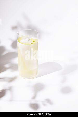 Ein eleganter und moderner Cocktail, der in einem hohen, klaren Glas mit einer großen Eisscherbe und zarten Tropfen hellgelben Öls serviert wird. Das d Stockfoto