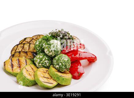Ein Teller umfasst eine Auswahl gegrillter Zucchini- und Auberginen-Scheiben sowie leuchtende rote Tomaten und grüne Kräuterkäsebällchen. Frisches Microgreens A Stockfoto