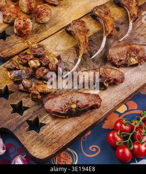 Eine Auswahl an köstlichen gegrillten Lammrippchen, Fleischbällchen und Kalbsschnitten ist auf rustikalen Holzbrettern angeordnet, die Sie genießen können Stockfoto