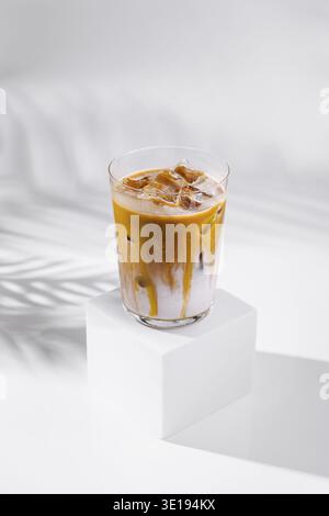Erfrischender Eiskaramell Latte steht auf einem weißen Würfel mit einem Palmblattschatten im Hintergrund Stockfoto
