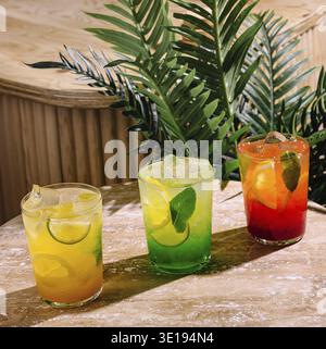 Drei farbenfrohe, erfrischende Sommercocktails mit Eis, Minzblättern und Zitrusfrüchten stehen auf der Bararbeitsfläche Stockfoto