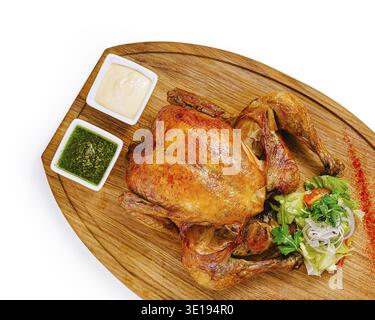 Gebratenes Huhn auf hölzernem Schneidebrett mit Gewürzen, Gemüse und Saucen, isoliert auf weißem Hintergrund Stockfoto