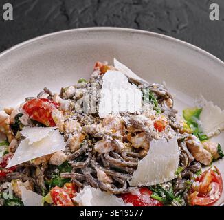 Schwarze Spaghetti mit Lachs, Spinat, Kirschtomaten und Parmesankäse auf einer weißen Platte Stockfoto