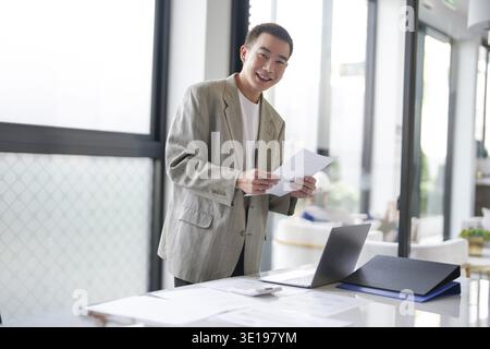 Lächelnder junger asiatischer Geschäftsmann im modernen Büro. Gutaussehender asiatischer Mann glücklich und freundlich während der Arbeit Erfolg Job Stockfoto