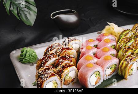 Auswahl an Sushi-Brötchen mit verschiedenen Belägen, serviert auf einem stilvollen Teller, komplett mit Essstäbchen und Sojasauce Stockfoto