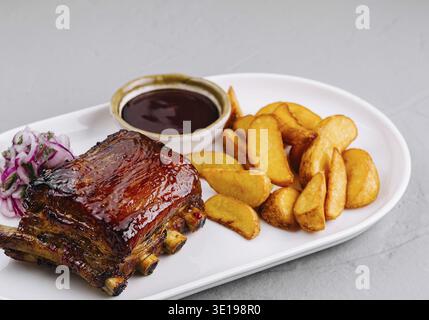 Köstlicher Teller mit glasierten Schweinerippchen mit Kartoffelscheiben, bbq-Sauce und Slaw auf einem weißen Teller Stockfoto