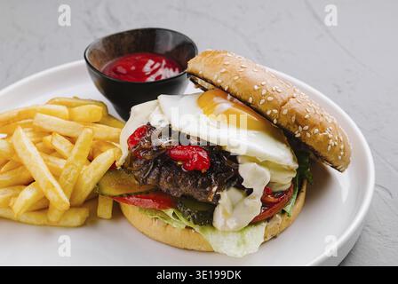 Gourmet-Burger mit Spiegelei, frischem Gemüse, serviert mit Pommes und Ketchup auf einem Teller Stockfoto
