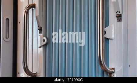 Schiebetür eines modernen Zuges, die metallische Griffe und blaue gewellte Oberfläche freigibt Stockfoto