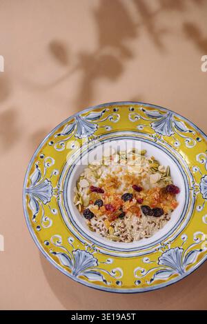 Blick von oben auf eine nahrhafte Müslimischung mit getrockneten Früchten und Nüssen in einer lebendigen Keramikschale vor pastellfarbenem Hintergrund Stockfoto